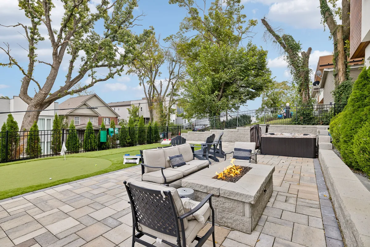 This exterior image showcases a landscaped backyard with a fire pit surrounded by comfortable seating, a putting green for casual games, and mature trees providing a welcoming outdoor atmosphere. The space is styled for both relaxation and playful activities, ideal for families and groups.