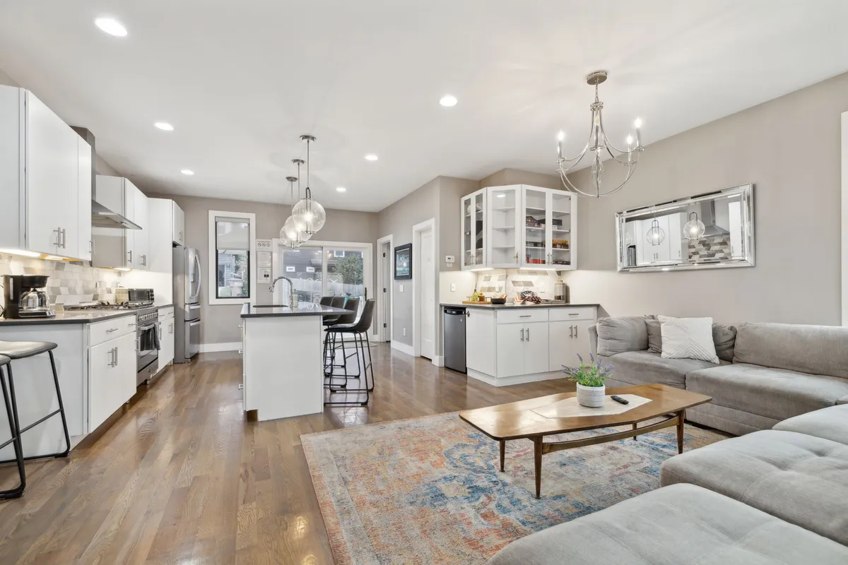 An open-concept living area that seamlessly integrates a cozy sofa, a stylish coffee table, and a view into the spacious kitchen. Modern light fixtures provide warmth, while the arrangement invites both relaxation and group gatherings. The kitchen island is visible, providing ample space for meal prep and socializing.