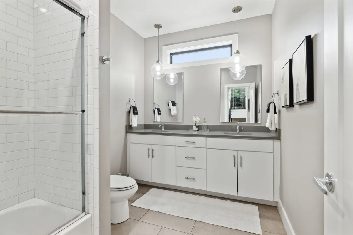 A contemporary full bathroom with a double vanity, large mirrors, glass-enclosed shower, and hanging light fixtures. The space is bright, airy, and evokes a spa-like atmosphere.