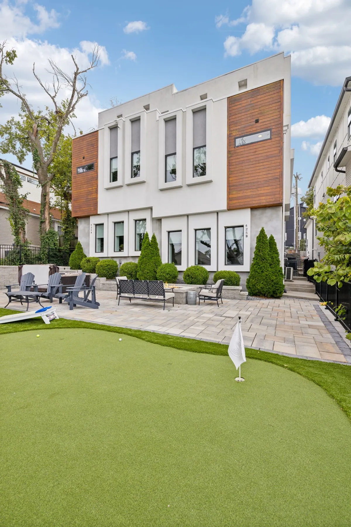 A modern exterior with sleek architectural lines, lush manicured landscaping, an inviting outdoor seating area, and a vibrant putting green. Friends can be seen gathering and enjoying activities such as a summer evening barbecue or a friendly putting competition, all bathed in natural light.
