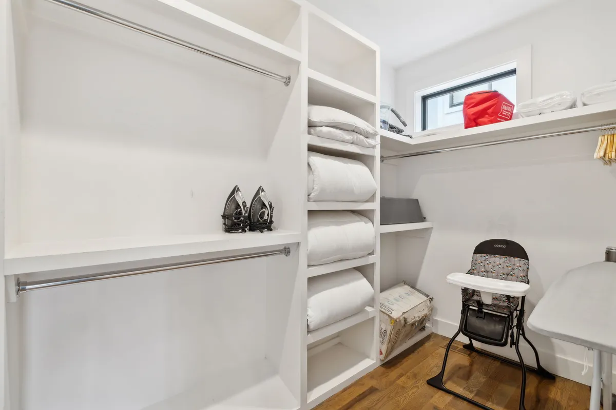 A practical laundry area, featuring bedding storage, an iron and ironing board, and a high chair. The setup is tidy and functional, indicating an in-unit washer/dryer and thoughtful amenities that support convenience during group stays.