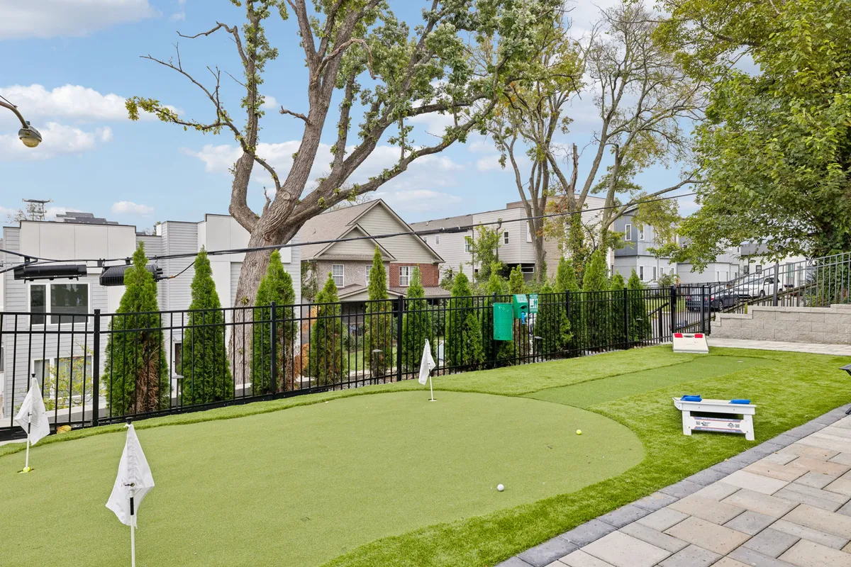 This playful exterior shot focuses on an artificial putting green, encircled by a secure fence and shaded by trees, with neighboring homes visible. The scene invites friendly competitions and leisurely afternoons outdoors.