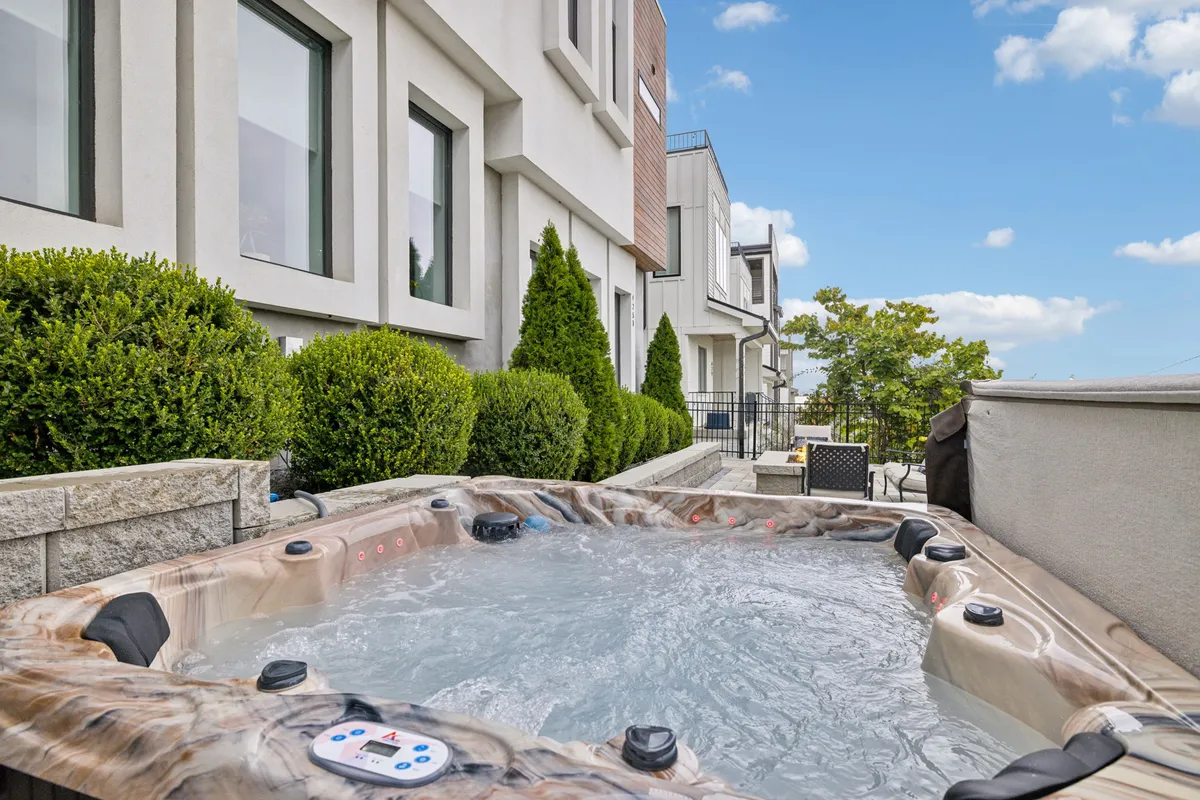The hero image showcases the inviting exterior of a modern townhome in Nashville, framed by lush hedges, with a steaming hot tub as the focal point. The outdoor space invites relaxation and group gatherings, especially during sunset, promising tranquil moments or lively celebrations. The scene hints at a blend of comfort, privacy, and fun, perfect for families or groups seeking a memorable getaway.