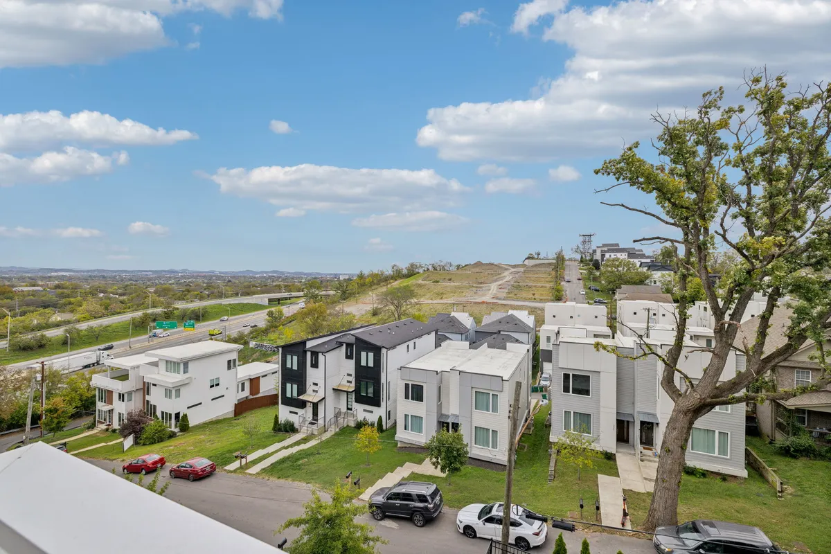 A serene view of a suburban neighborhood with modern houses, a winding road, and a green lawn stretching toward distant hills. The peaceful setting conveys easy access to local parks and safe streets for family walks, biking, or exploring nearby attractions.