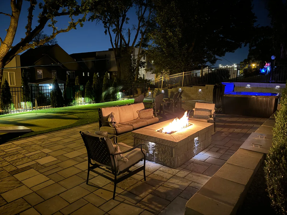 This exterior image highlights a cozy fire pit area with comfortable outdoor seating, complemented by a swimming pool visible in the background. The setting is perfect for groups to gather in the evening, enjoy relaxing conversations around the fire, or unwind after a day of activities.