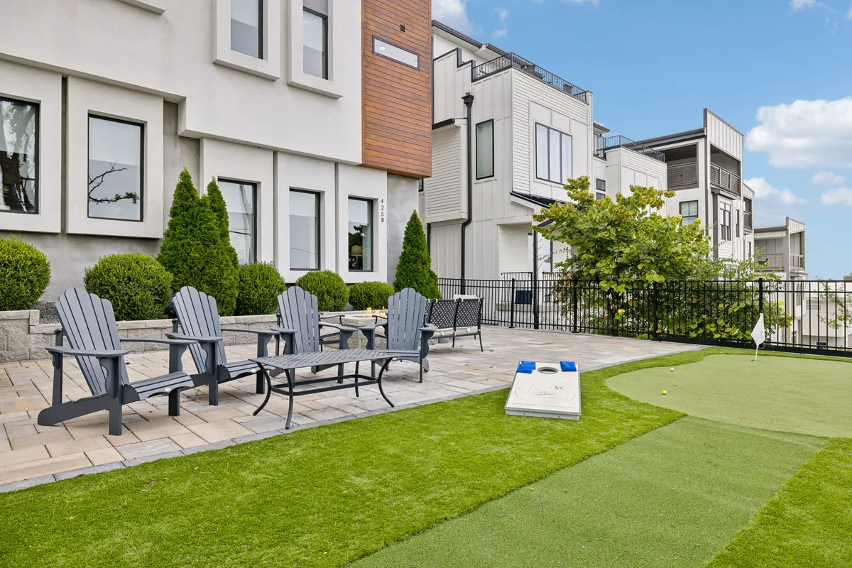 A relaxed backyard scene showcases a comfortable outdoor seating area beside a golf putting green. The space is surrounded by manicured landscaping, inviting guests to enjoy friendly competitions or unwind while soaking up the sunset.