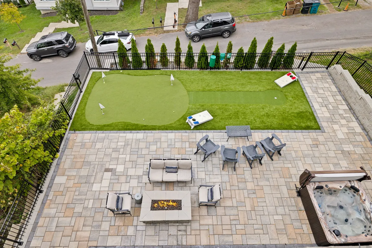 This vibrant exterior shot showcases a backyard oasis featuring a putting green, a cozy fire pit area surrounded by seating, and a private hot tub nestled conveniently nearby. The space is clearly designed for group gatherings, with multiple amenities in one frame, all set against manicured landscaping and modern outdoor furnishings.